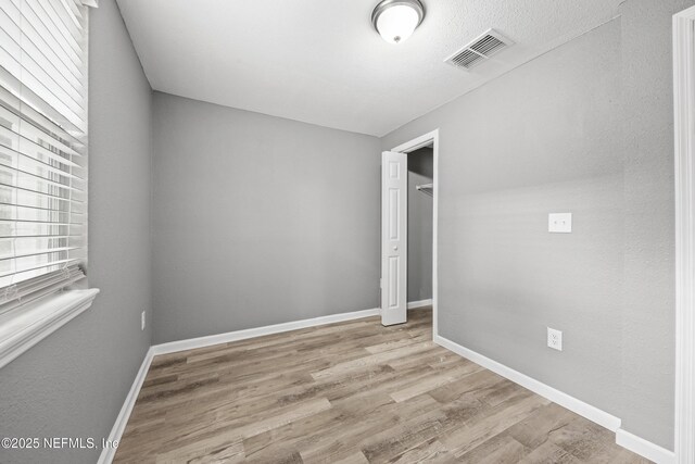 unfurnished bedroom with a closet, light wood-type flooring, a textured ceiling, and multiple windows