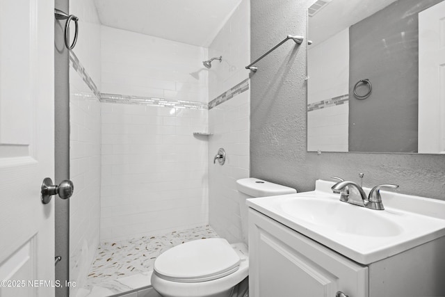 bathroom featuring a tile shower, vanity, and toilet