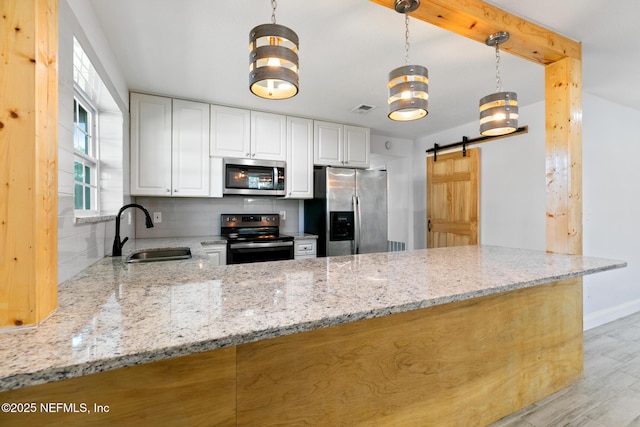 kitchen featuring white cabinets, sink, a barn door, light stone countertops, and appliances with stainless steel finishes