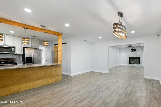 kitchen featuring backsplash, light hardwood / wood-style flooring, light stone countertops, a fireplace, and appliances with stainless steel finishes