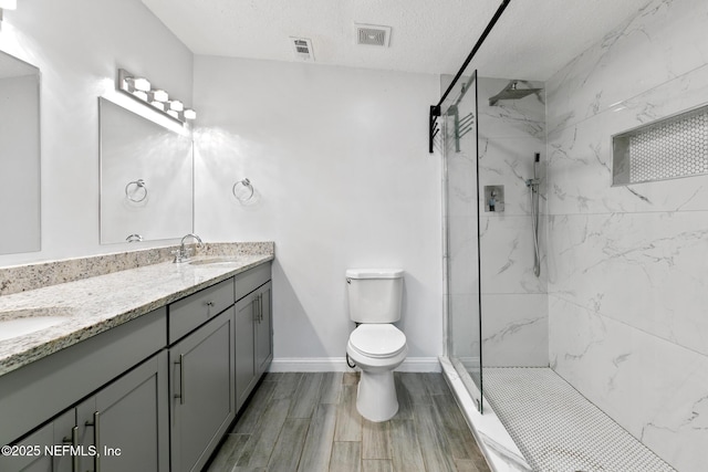 bathroom featuring a tile shower, vanity, a textured ceiling, and toilet