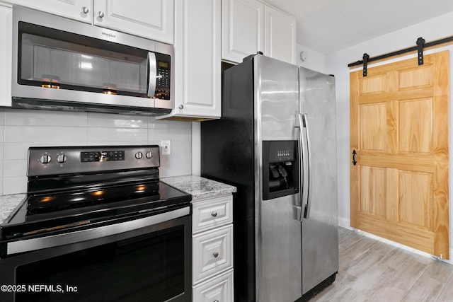 kitchen with light stone countertops, tasteful backsplash, a barn door, white cabinets, and appliances with stainless steel finishes