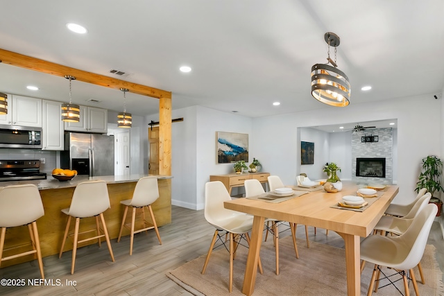 dining room with beam ceiling, light wood-type flooring, a stone fireplace, and ceiling fan