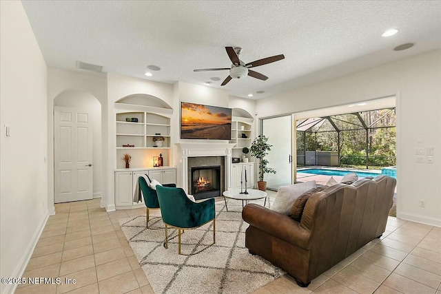 living room with ceiling fan, light tile patterned floors, built in features, and a textured ceiling