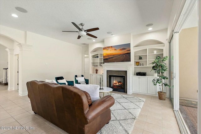 living room featuring ornate columns, light tile patterned floors, ceiling fan, a textured ceiling, and built in shelves