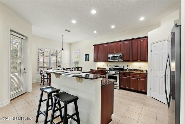 kitchen featuring a breakfast bar area, decorative light fixtures, light tile patterned floors, dark stone countertops, and appliances with stainless steel finishes