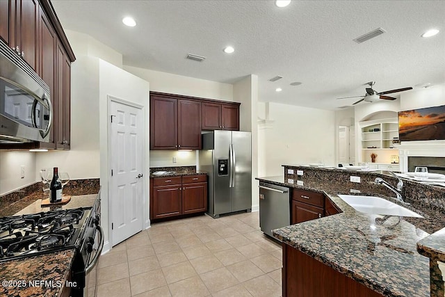 kitchen featuring appliances with stainless steel finishes, sink, dark stone counters, a textured ceiling, and built in shelves