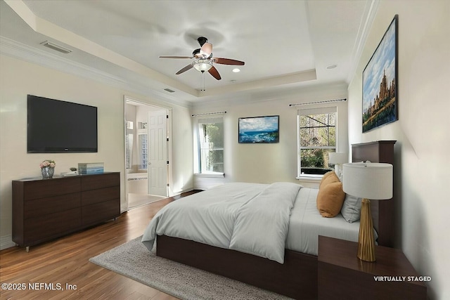 bedroom with hardwood / wood-style flooring, ensuite bathroom, crown molding, and a raised ceiling