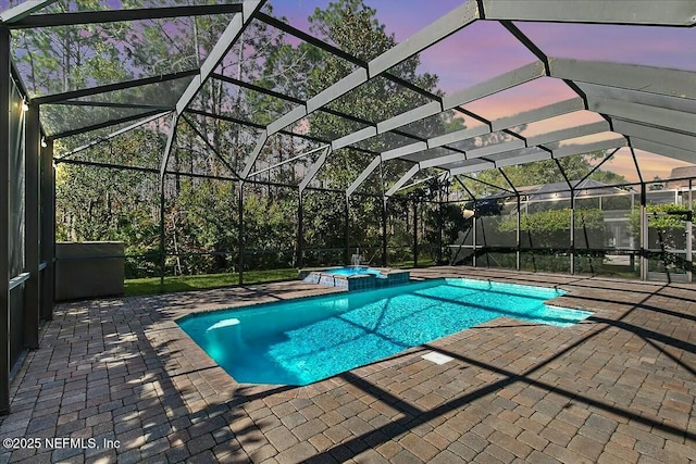 pool at dusk with an in ground hot tub, glass enclosure, and a patio area