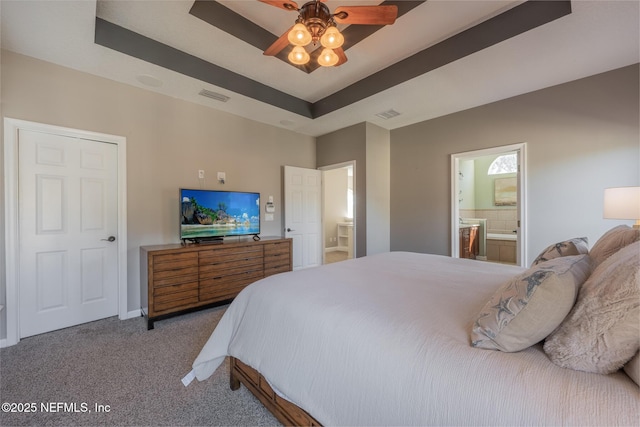 bedroom with a raised ceiling, connected bathroom, ceiling fan, and carpet flooring