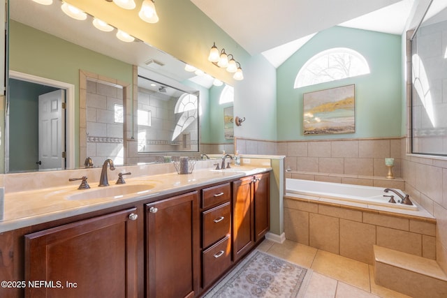 bathroom with tiled tub, tile patterned flooring, vanity, and lofted ceiling