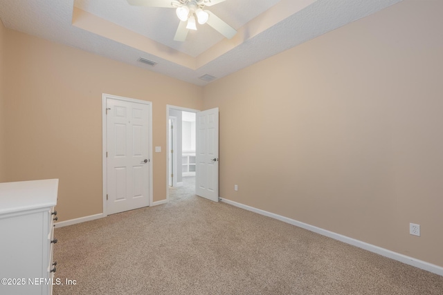 carpeted empty room featuring ceiling fan and a raised ceiling