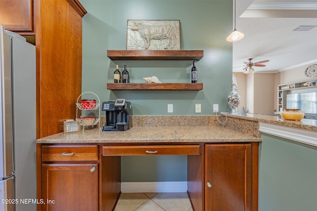 kitchen featuring ceiling fan, built in desk, ornamental molding, light stone counters, and stainless steel refrigerator