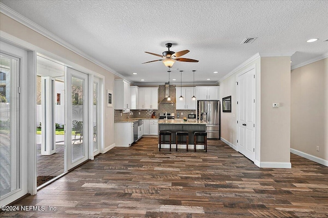 kitchen featuring appliances with stainless steel finishes, wall chimney exhaust hood, decorative light fixtures, white cabinetry, and a kitchen island