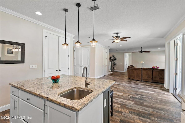 kitchen featuring pendant lighting, white cabinets, sink, light stone countertops, and an island with sink