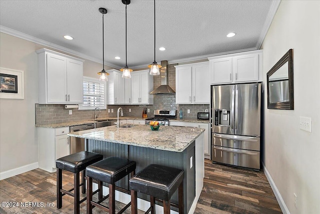 kitchen with white cabinetry, wall chimney range hood, crown molding, an island with sink, and appliances with stainless steel finishes