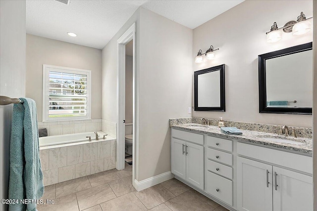 bathroom featuring tile patterned floors, vanity, a textured ceiling, tiled bath, and toilet