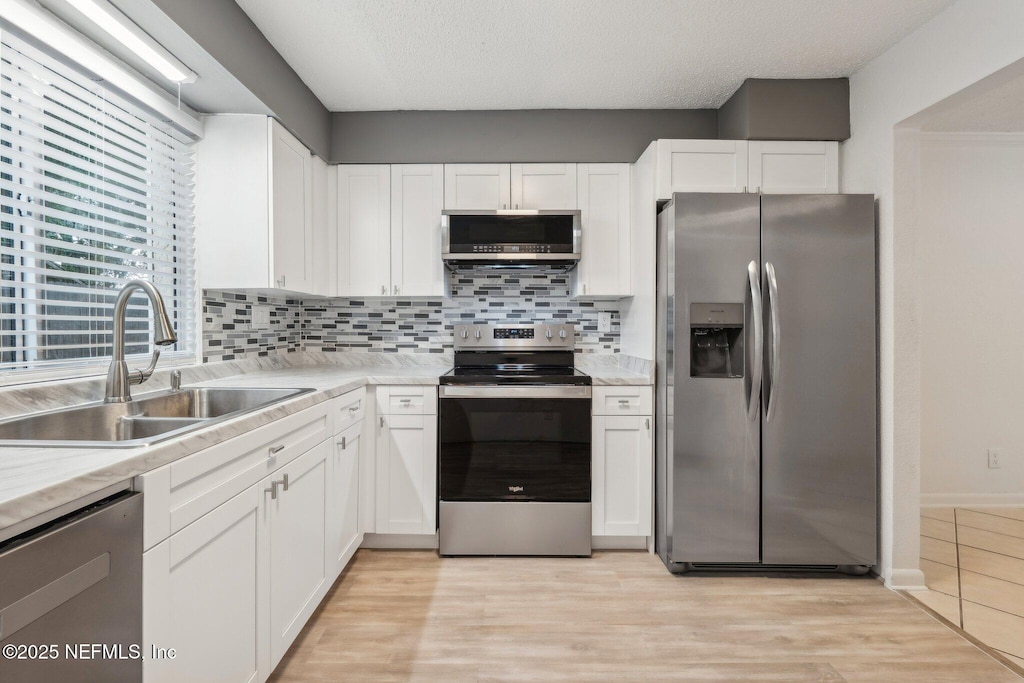 kitchen with tasteful backsplash, sink, white cabinets, and appliances with stainless steel finishes