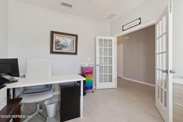 office area with french doors, light hardwood / wood-style floors, and a textured ceiling