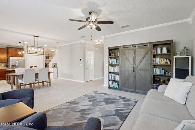 living room featuring ceiling fan, a barn door, crown molding, light hardwood / wood-style floors, and a textured ceiling