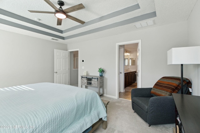 bedroom with ceiling fan, a raised ceiling, ensuite bathroom, a textured ceiling, and light carpet