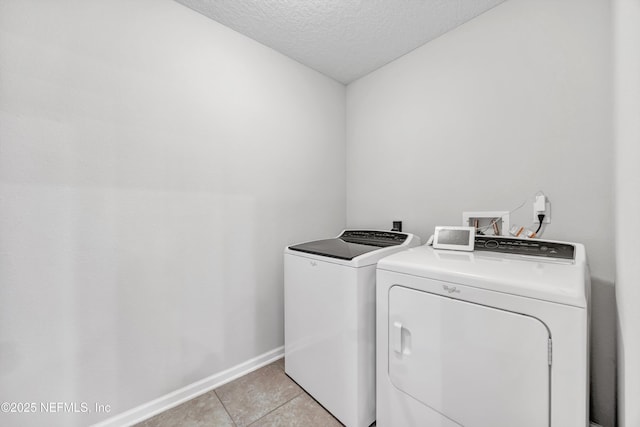 clothes washing area with washing machine and dryer, light tile patterned floors, and a textured ceiling