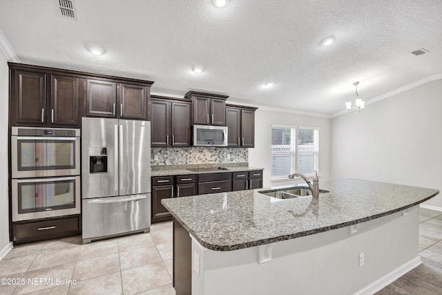 kitchen featuring decorative backsplash, dark brown cabinets, stainless steel appliances, sink, and a center island with sink