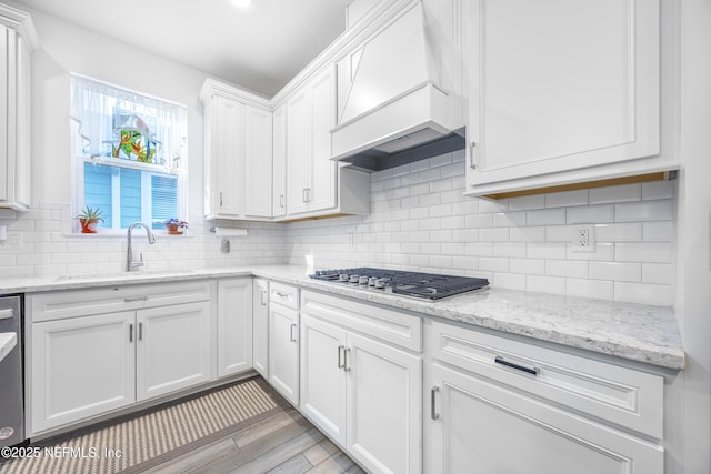 kitchen with premium range hood, white cabinets, sink, decorative backsplash, and appliances with stainless steel finishes