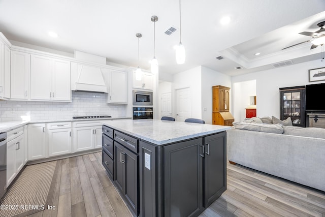 kitchen with appliances with stainless steel finishes, custom exhaust hood, a tray ceiling, pendant lighting, and white cabinetry