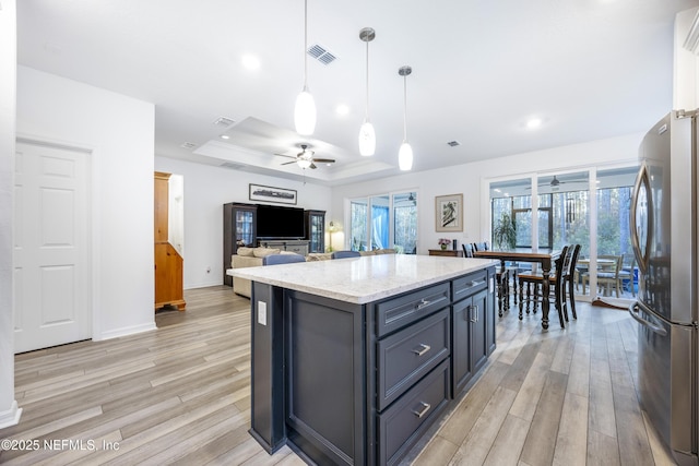 kitchen with stainless steel refrigerator, ceiling fan, pendant lighting, a tray ceiling, and a kitchen island