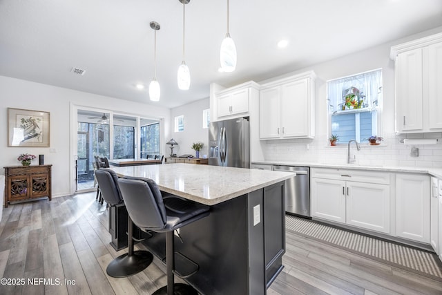 kitchen featuring hanging light fixtures, white cabinets, stainless steel appliances, and a kitchen island