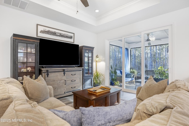 living room with wood-type flooring, a tray ceiling, ceiling fan, and ornamental molding