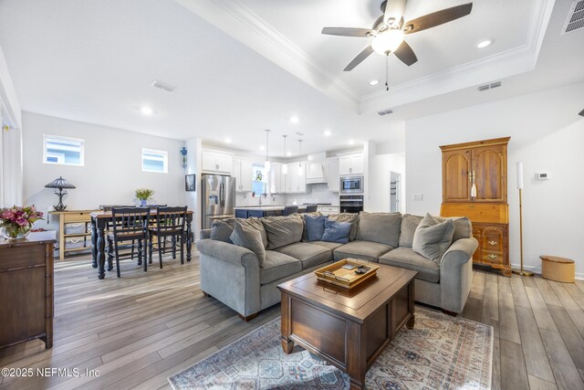 living room featuring light wood-type flooring, a tray ceiling, ceiling fan, and sink