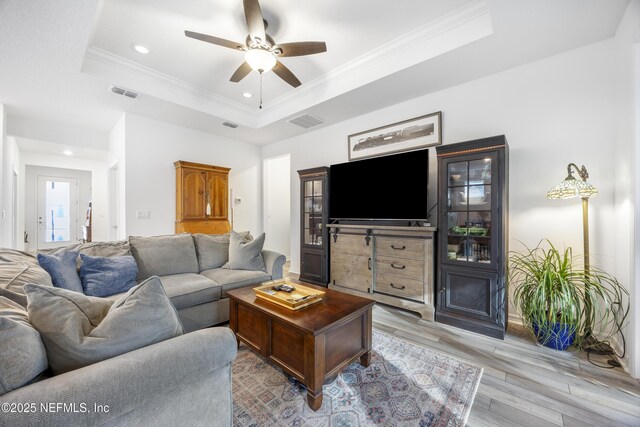 living room with ceiling fan, light hardwood / wood-style floors, a raised ceiling, and crown molding