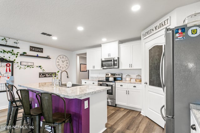 kitchen with sink, white cabinets, stainless steel appliances, and a center island with sink