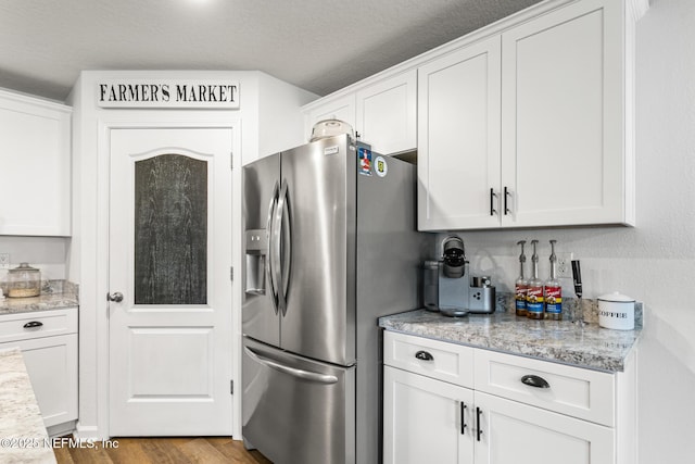 kitchen with white cabinets, light wood-type flooring, a textured ceiling, light stone counters, and stainless steel fridge with ice dispenser