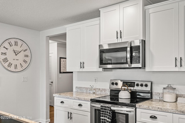 kitchen with light stone countertops, appliances with stainless steel finishes, a textured ceiling, and white cabinetry