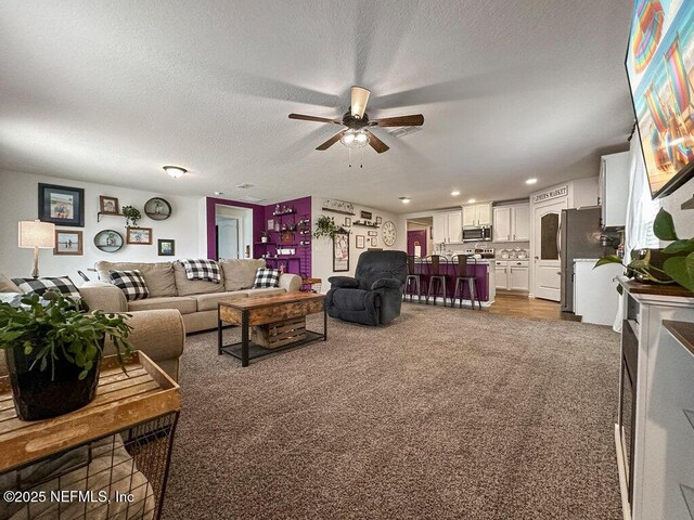 living room with ceiling fan, dark carpet, and a textured ceiling