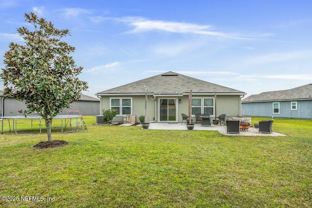 rear view of property with a lawn, a patio area, a trampoline, and an outdoor fire pit