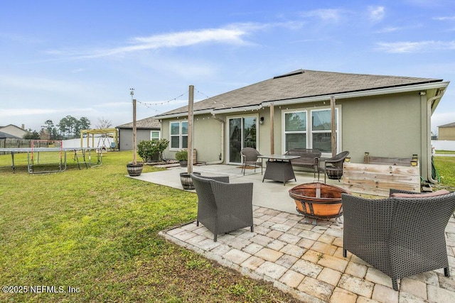 back of house with a trampoline, a fire pit, a patio area, and a lawn