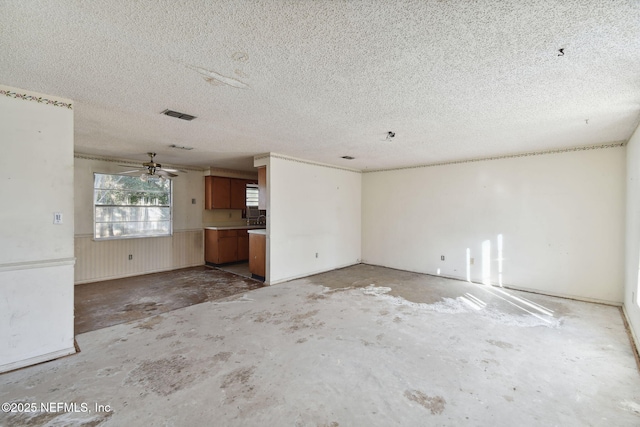 unfurnished living room featuring ceiling fan, wooden walls, concrete flooring, and a textured ceiling