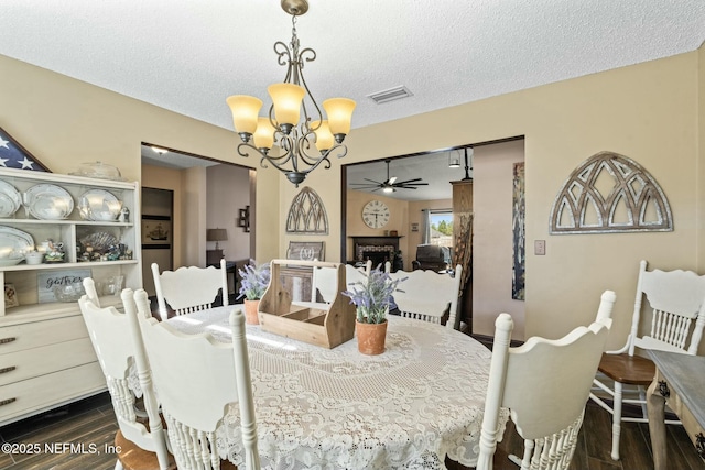 dining area featuring ceiling fan with notable chandelier, a textured ceiling, and dark hardwood / wood-style floors