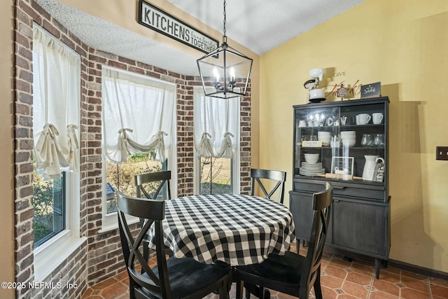 dining room with brick wall, a notable chandelier, and vaulted ceiling