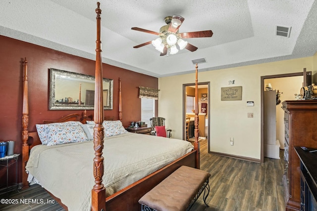 bedroom with a textured ceiling, a fireplace, dark hardwood / wood-style floors, ceiling fan, and a tray ceiling