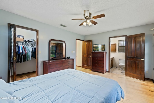 bedroom featuring a textured ceiling, a spacious closet, ensuite bathroom, a closet, and ceiling fan