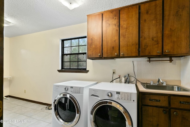 laundry area with sink, a textured ceiling, washer and dryer, and cabinets