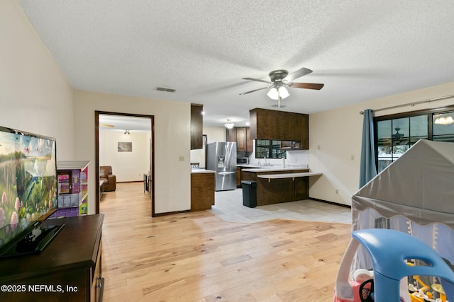 interior space with appliances with stainless steel finishes, light hardwood / wood-style floors, kitchen peninsula, ceiling fan, and a textured ceiling