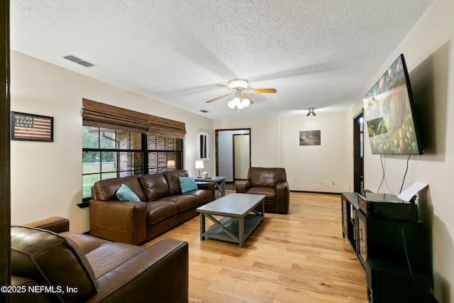 living room featuring light wood-type flooring, ceiling fan, and a textured ceiling