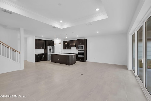 kitchen with wall chimney exhaust hood, sink, appliances with stainless steel finishes, a tray ceiling, and a kitchen island