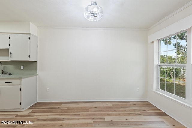 unfurnished dining area with light wood-type flooring, a wealth of natural light, a notable chandelier, and sink